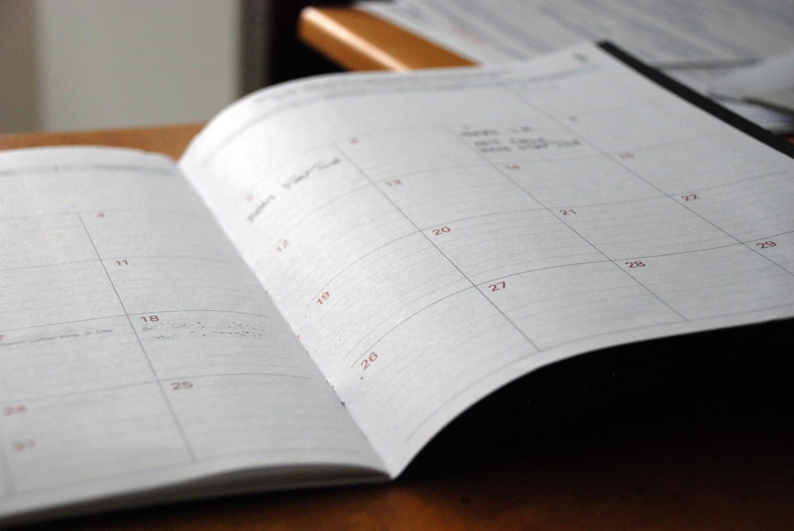 Open monthly paper planner on a wooden desk with handwritten entries