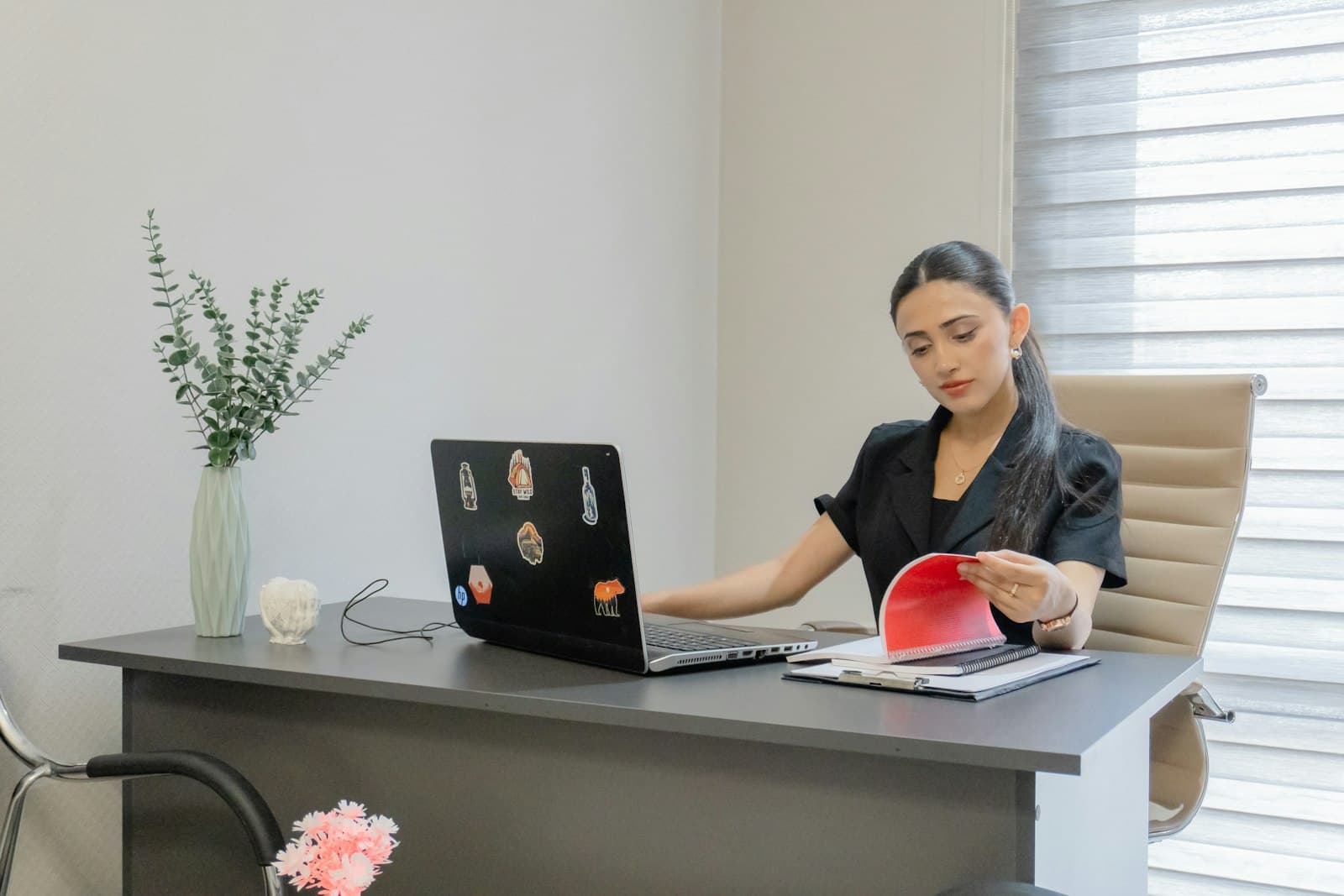 Office manager turning pages of a ledger beside an open laptop at a desk